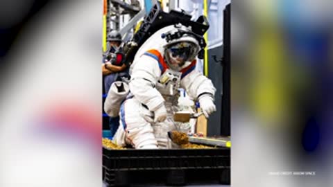 An astronaut in a space suit works with soil in a simulation container.