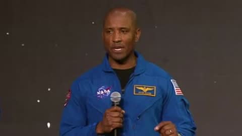 NASA astronaut speaking in blue flight suit on stage