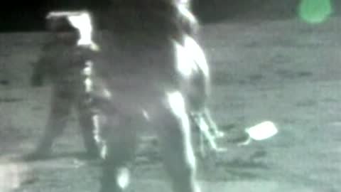 Archival grainy footage shows astronauts working near equipment on the moon.