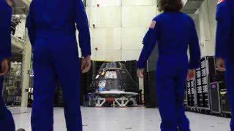 NASA astronauts walking toward Orion spacecraft in cleanroom facility