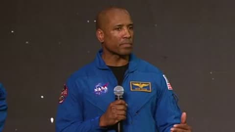 NASA astronaut speaking on stage with dark background