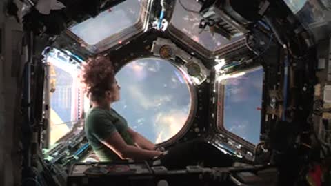 Astronaut inside spacecraft looking out circular window at Earth.