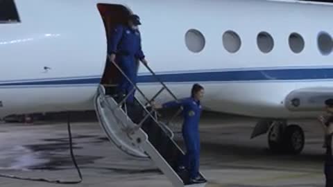 Astronauts descending stairs from private jet on tarmac.