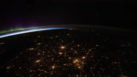 Earth's limb glowing green with city lights visible below in darkness.