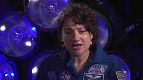 A woman in a blue NASA jumpsuit speaking in an interview setting