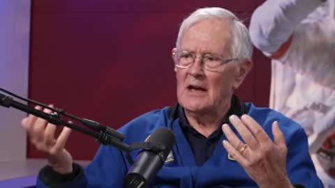 An elderly man speaking and gesturing during an interview