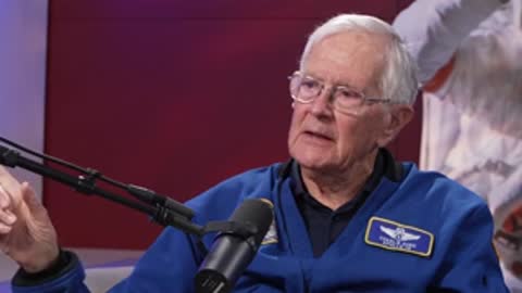 An elderly man speaking with hand gestures during a seated interview