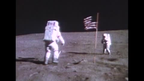 Apollo 16 astronaut walking near American flag on moon surface
