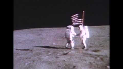 Two Apollo 16 astronauts working near American flag on lunar surface