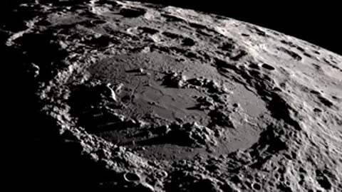 A detailed black-and-white aerial view of a large crater on the moon's surface.