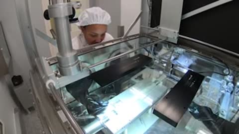 A technician works inside a specialized enclosure with robotic arms and lighting.