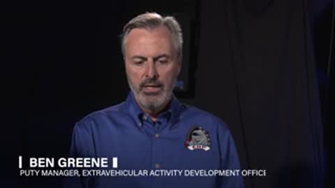 A man with a grey beard speaks during an interview wearing a blue shirt.