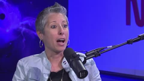 A woman with short grey hair speaks animatedly during a studio interview.