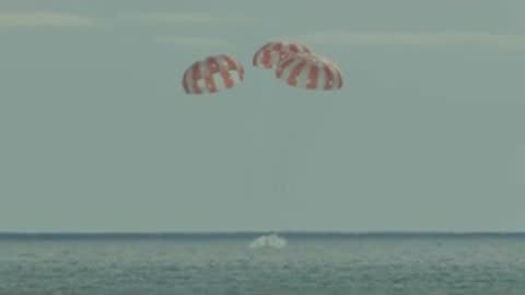 Parachutes descend and land in the calm sea.