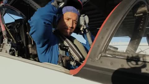 An astronaut puts on a helmet while sitting in the cockpit of a jet.