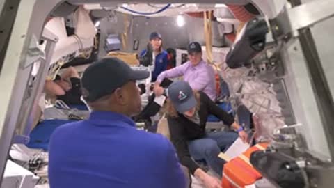Astronauts and support staff work inside a spacecraft mockup.