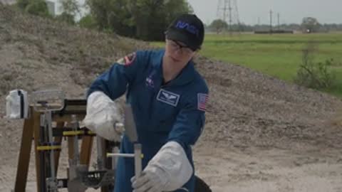 An astronaut in a blue jumpsuit operates equipment outdoors.
