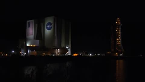 Lunar surface view juxtaposed with Kennedy Space Center at night