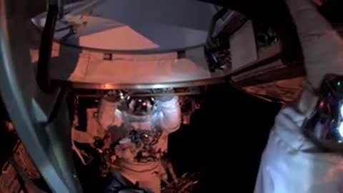 View from inside a spacecraft looking out at an astronaut working in space.