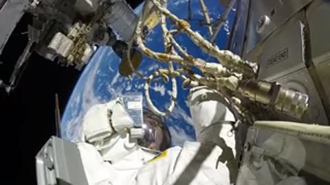 An astronaut works with equipment outside the space station with Earth below.