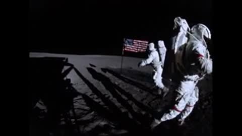 Astronaut in spacesuit walks on lunar surface near American flag in archival footage.
