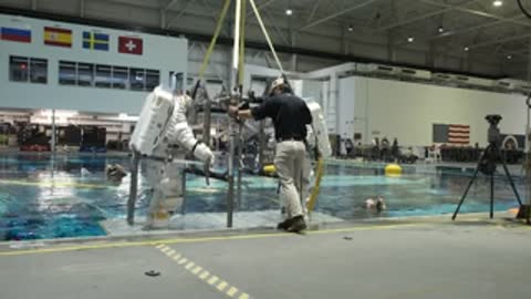 Astronaut lowers into Neutral Buoyancy Laboratory pool using crane system.