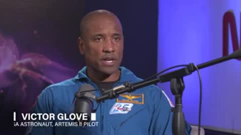 Astronaut in blue uniform speaks during interview with microphone visible.
