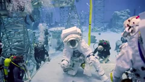 Astronauts and divers conduct underwater training operations around simulated lunar rocks.