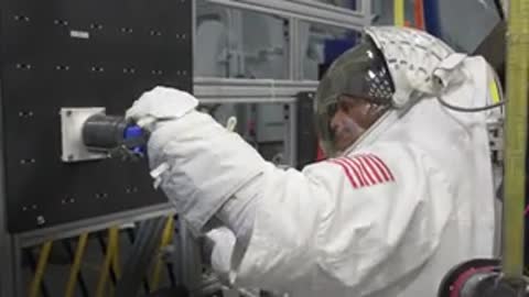 Astronaut operates mechanical test rig device in indoor industrial facility setting.
