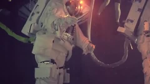 Astronauts in spacesuits work together underwater, handling hoses and equipment connections.
