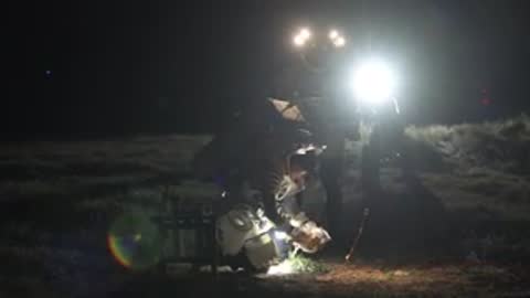 Astronaut uses floodlight equipment outdoors at night during field test simulation.