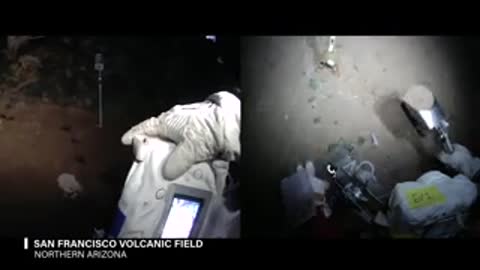 Astronaut uses handheld device and tool outdoors at night in field environment.
