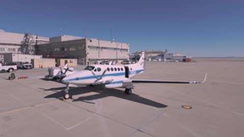 A white and blue NASA airplane parked on an airport tarmac.