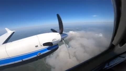 View of the airplane engine and propeller in flight above clouds.