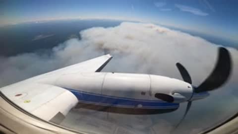 aerial view from airplane window of a thick smoke plume rising from a forest fire