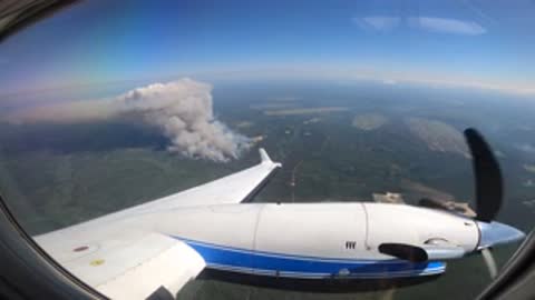 aerial view from an airplane of a distant wildfire plume over forested landscape
