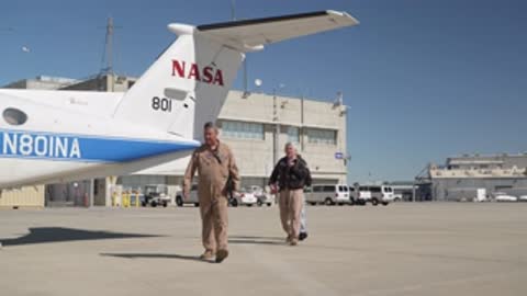 Ground crew walking toward the parked NASA airplane on tarmac.