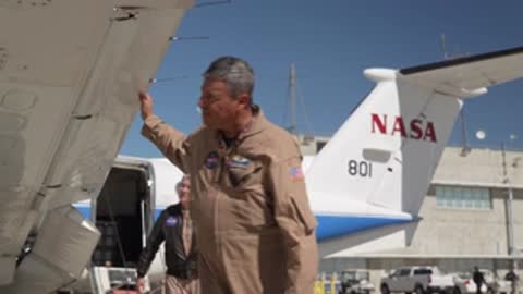 A man in a jumpsuit inspecting the wing of the airplane.