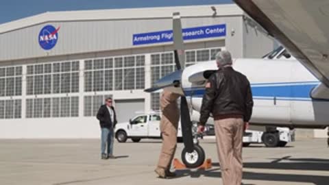 Two crew members inspecting the front landing gear of the airplane.