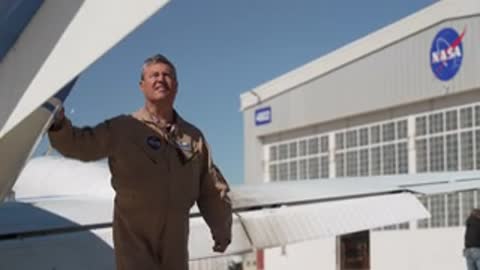 A man in a flight suit walking around the airplane wing.