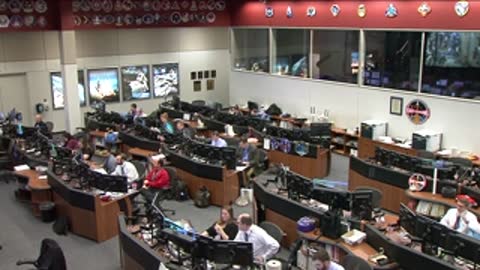 Wide view of personnel working in the brightly lit Flight Control Room.