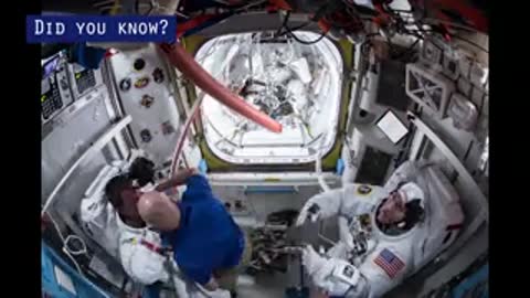 Astronauts preparing white spacesuits inside the International Space Station in microgravity.