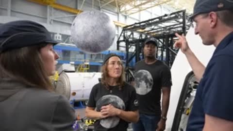 Instructor pointing while discussing equipment beneath a hanging model moon.