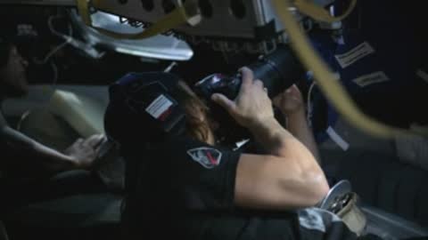 Astronaut working with camera equipment inside a spacecraft cabin simulator.