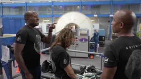 Two people talk in a hangar near a spacecraft mockup.