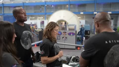 Three people converse in a large facility with spacecraft mockups.