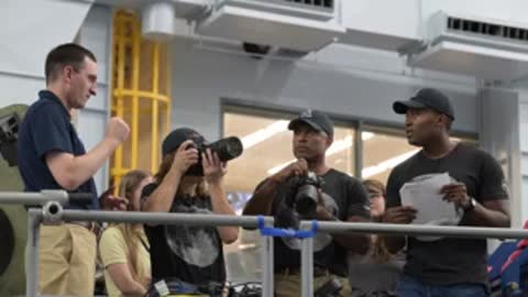 Astronauts and instructors reviewing paper documents and a camera by a railing.