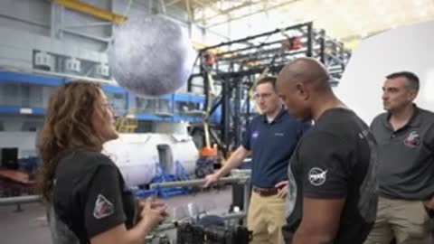 A woman speaks to astronauts near a hanging moon model.