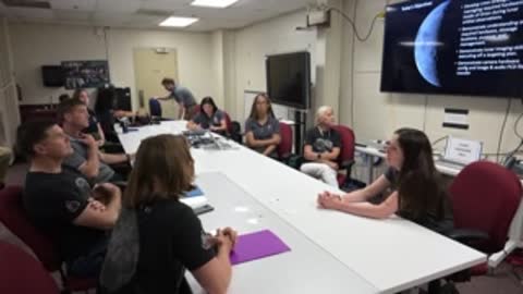 Astronauts and trainers sit around a conference table listening.