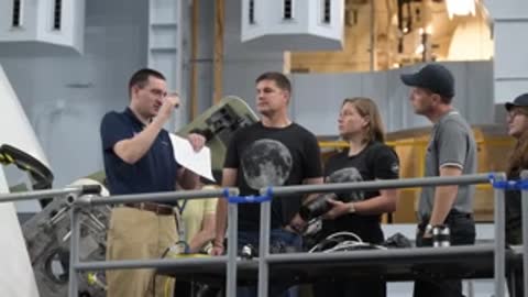 Astronauts stand on an elevated platform discussing camera equipment.